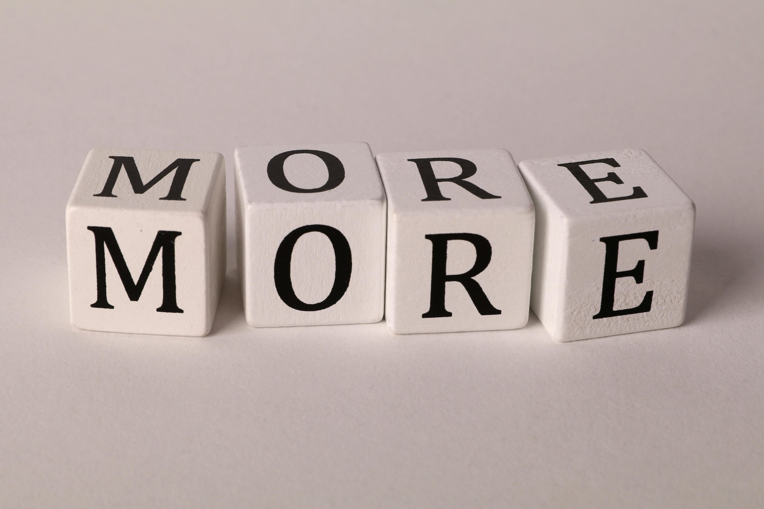 Close-up view of four dice with letters spelling MORE on a white background.