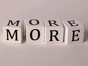 Close-up view of four dice with letters spelling MORE on a white background.